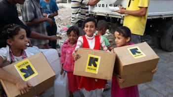 Little kids hold boxes with the International Rescue Committee provisions
